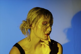 Woman in yellow light with wet hair in front of blue background, thoughtful pose with shadow, photo