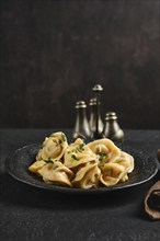 A black stone plate holds freshly made dumplings garnished with parsley, creating a delightful dish