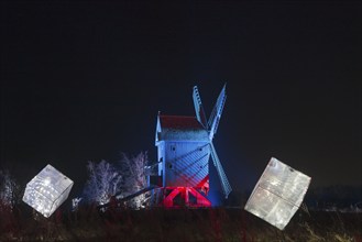 An illuminated windmill with abstract cubes in the foreground at night, world of lights,