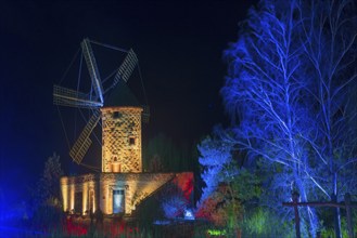 Historic stone mill at night, illuminated in blue, surrounded by trees, world of lights,