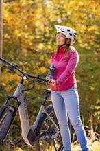 Woman pushing ebike through autumn forest, Black Forest, Gechingen, Germany, Europe