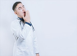 Young sleepy doctor yawning on isolated background. Tired of working doctor concept. Tired and