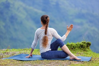 Hatha yoga outdoors, sporty fit woman doing yoga asana Parivrtta Marichyasana (or ardha