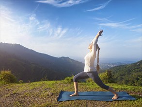 Yoga outdoors, sporty fit woman doing yoga asana Virabhadrasana 1, Warrior pose posture outdoors in