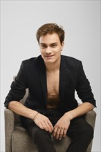 Young man in black suit siting in an armchair in the studio