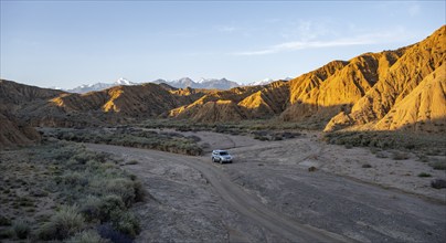 Off-road vehicle driving through a canyon, landscape of eroded hills at sunrise, badlands, white