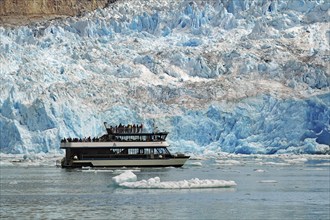 Passenger boat in front of the front of a glacier calving into the sea shimmering bluish, Tracy Arm