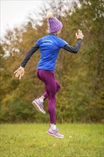 A dynamic rear view of a woman jogging in autumn forest, Gechingen, Black Forest, Germany, Europe