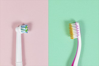 Comparison of electronic and traditional toothbrush side by side on pink and green background