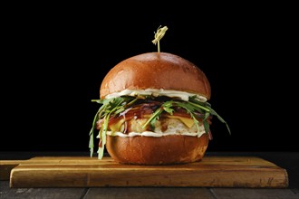 Burger with chicken patty teriyaki sauce on wooden serving board over black background