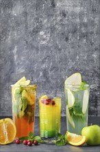 Three glasses with fruit refreshing drink on gray shabby background