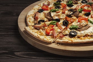 Ham pizza with (capsicum), mushrooms, olives and basil leaves on wooden board on old table close up