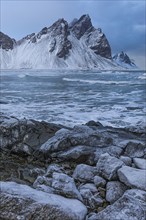 Iced rocks on the beach of Stokkness, behind them the snowy rocky slopes of Vestrahorn, near Höfn,