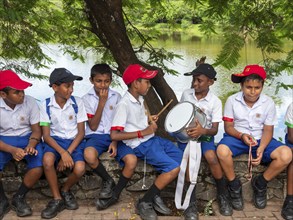 School children school uniform sitting on wall and drumming, Sri Lanka, Asia