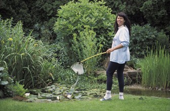 Woman fishing algae from garden pond, Germany, Europe