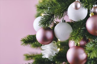 Close up of decorated Christmas tree with white seasonal and pink tree ornaments like baubles and