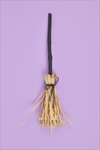 Witch broom with black twig and straw bristles on violet background