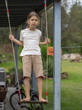 Boy swinging standing on children's swing at shed, Germany, Europe