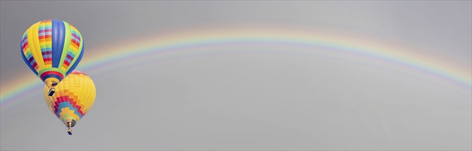 Hot air baloons drift with rainbow in the sky