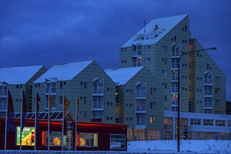 Illuminated supermarket at dawn, behind it apartment buildings in modern architecture, Reykjavik,