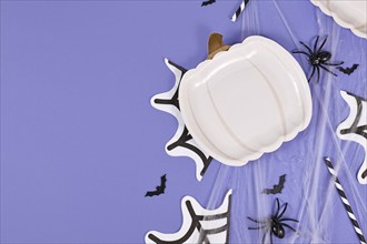 Halloween party flat lay with pumpkin shaped plate, spiders, bats and spiderwebs on violet