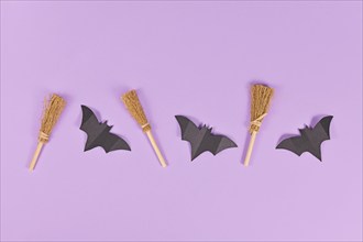 Halloween paper bats and witch brooms in a row on purple background