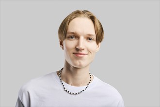 Closeup portrait of smiling young man in white t-shirt over grey studio background