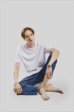 Young barefoot man sits on the floor in studio in t-shirt and jean