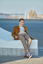 Spring, autumn outfit. Street fashion. Young man in checkered trousers, sweater and wool coat