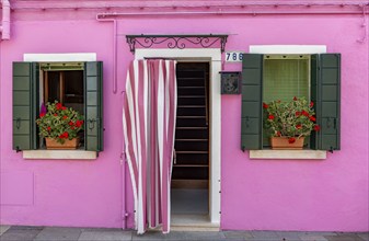 Pink house facade with entrance door and windows with flowers, colourful houses on the island of