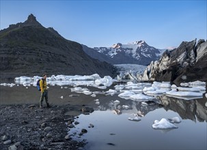 Hikers at a lake, reflection in the Svínafellslon glacier lagoon with ice floes, Svínasfellsjökull