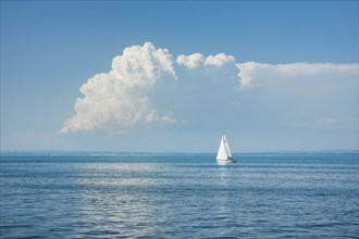 White sailboat on the turquoise water of Lake Constance with a low, large spring cloud in the