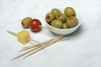 Green olives stuffed with pepper pieces, in bowl, toothpick with olive and cheese cube