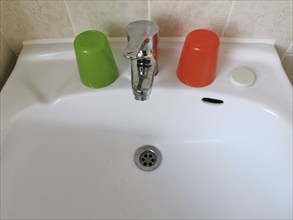 Washbasin with colourful plastic toothbrush cups and a bar of soap in a primitive hotel