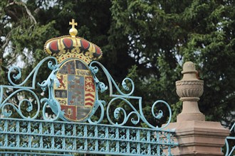 Ornate metal grille with golden crown to the entrance in castle park, coat of arms, turquoise,