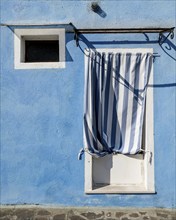 Blue house facade with entrance door with blue and white curtain and window, colourful houses on