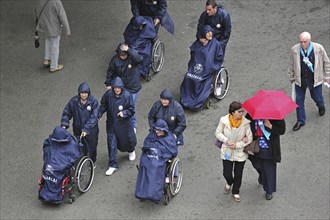 Disabled people in wheelchairs in the rain visiting Sanctuary of Our Lady of Lourdes, Pyrenees,