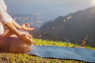 Close up of woman in Padmasana yoga lotus pose with chin mudra outdoors with copyspace. With light