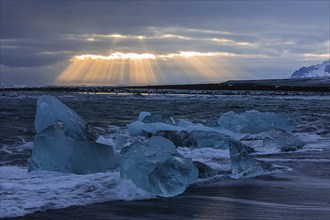 Waves breaking on icebergs on the black beach of Breidamerkursandur, sunset, near Jökullsarlon,