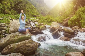 Woman doing yoga meditation asana Padmasana lotus pose outdoors at tropical waterfall