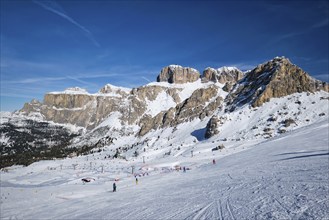 View of a ski resort piste with people skiing in Dolomites in Italy. Ski area Belvedere. Canazei,