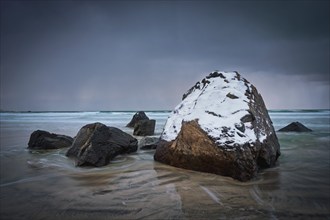 Rocks covered with snow on Norwegian sea beach in fjord in stormy weather with clouds. Skagsanden