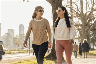 Two women jog side by side in a sunlit park, smiling as they embrace an active lifestyle.