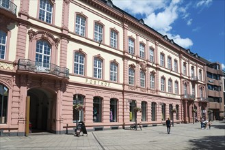 Historic building in pink and beige in the city centre with pedestrians under a blue sky, Posthof