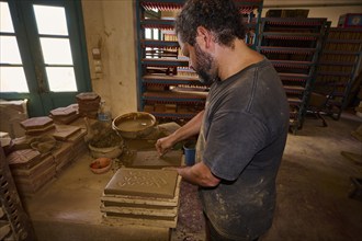 Man moulding clay bricks in a traditional pottery workshop with natural light, Brickworks Patmos