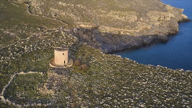 Drone shot, Lindos, late afternoon light, drone view of an old windmill on a rocky shore in the