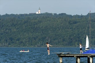 Boy and girl bathing in the lake, children jumping over diving board into the water, jetty of