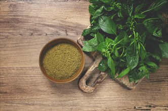 Ground green basil, in a ceramic bowl, with a bouquet of fresh green basil, on the table, top view,