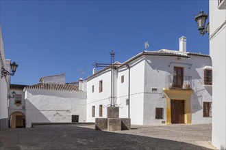 A sunny alleyway with white traditional buildings and cobbled streets under a clear blue sky,