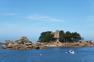 Rocky island with historic architecture and trees, surrounded by blue water with a small boat,